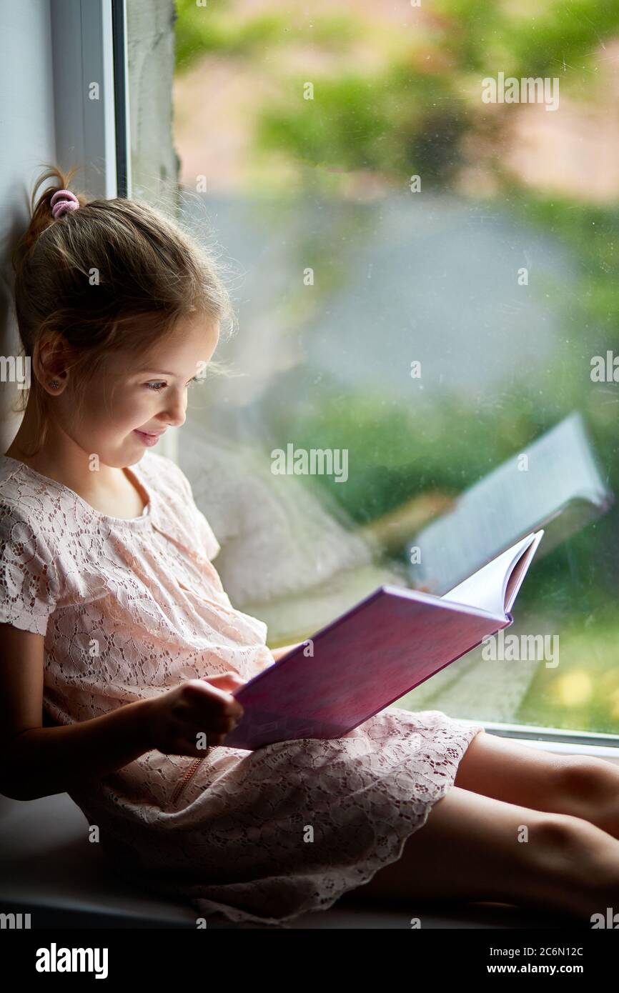 Cute little girl reading book at home, at windowsill Stock Photo - Alamy