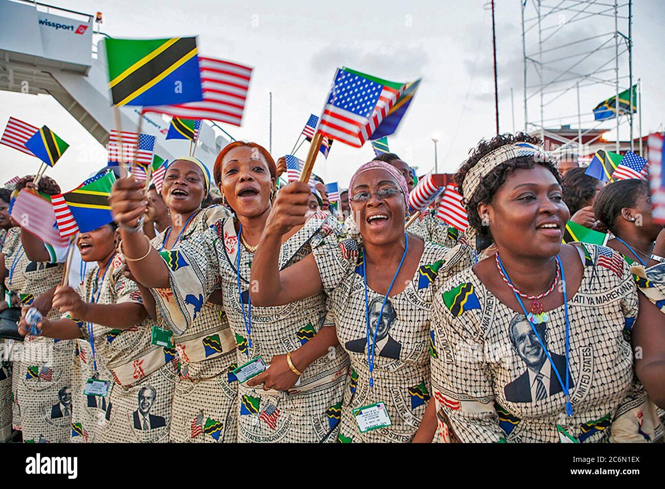 Tanzanian women in dresses bearing the likeness of President George W. Bush wave flags from Tanzania and the United States as they await the arrival of President George W. Bush and Mrs. Laura Bush Saturday, Feb. 16, 2008, to Julius Nyerere International Airport in Dar es Salaam. Stock Photo