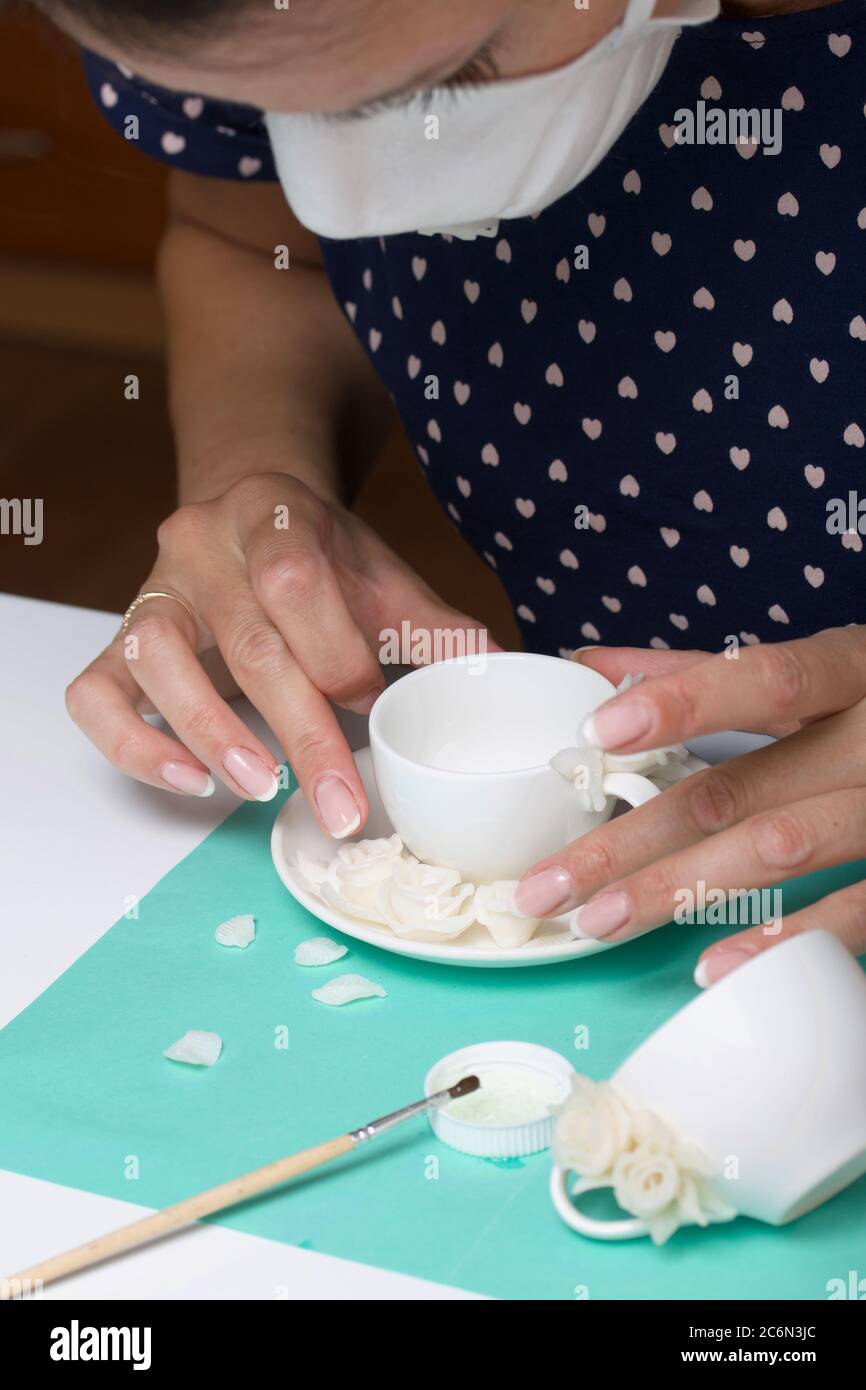Roses with petals made of white polymer clay. A woman sticks them on a mug. Crafts from polymer clay. Stock Photo