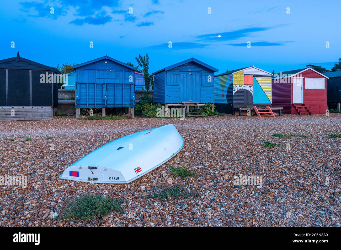 Moonrise behind the colourful beach huts on West Beach in Whitstable, Kent. Stock Photo