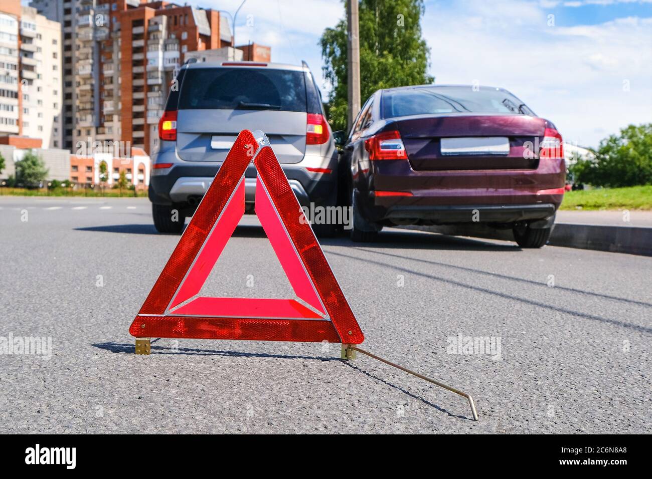 Triangular red retro-reflective sign of accident on the road. Collision of two cars. Broken bumper and hood. Car accident on the street. Stock Photo