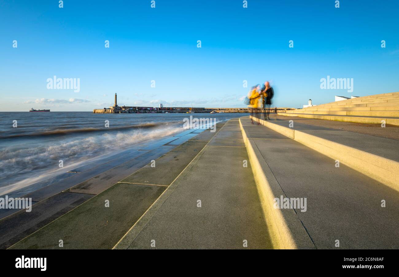 A couple walk on the steps at Margate seafront with the harbour arm in the background. Stock Photo