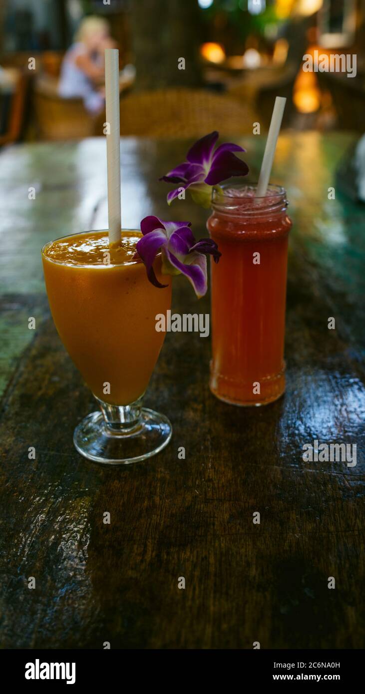 Glass of orange drink on wooden table in cafe. Tasty appetizing flower decorated orange drink in glasses with straw on wooden table in outside cafe Stock Photo