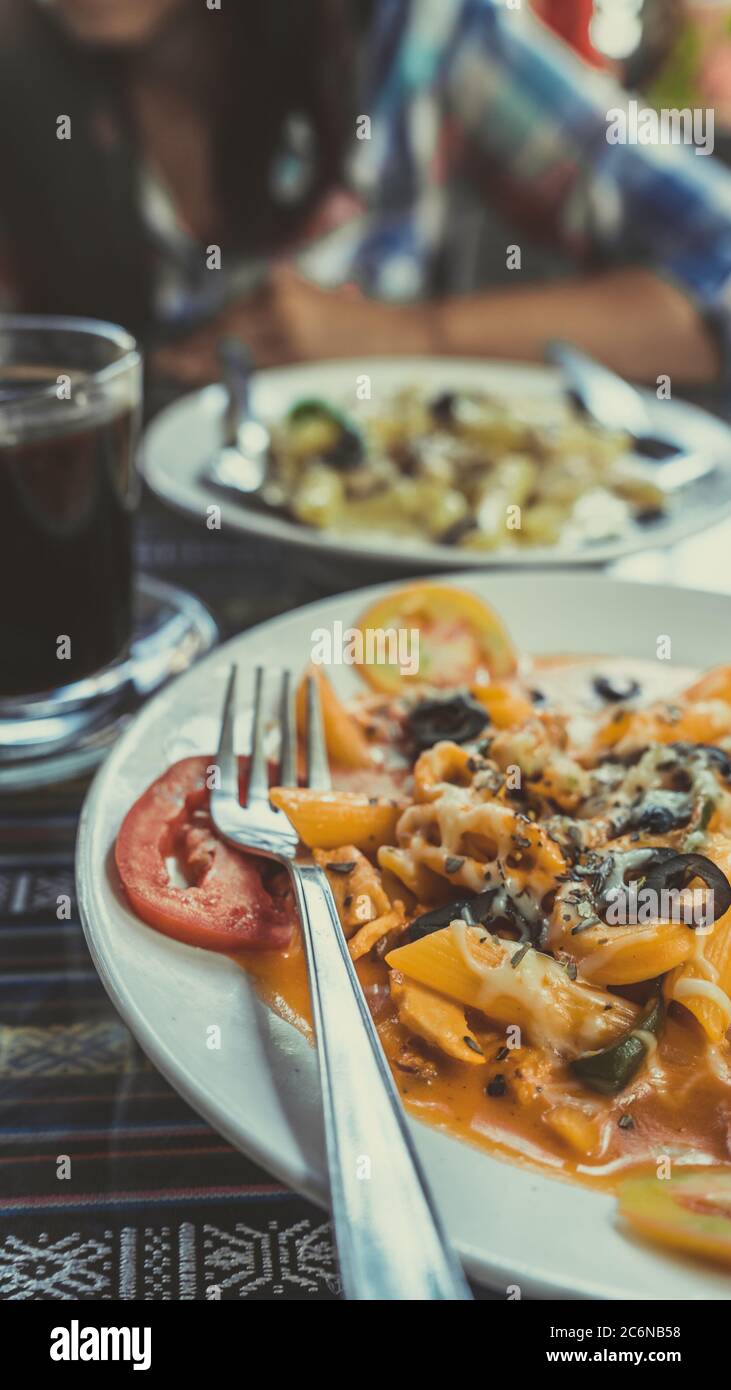 Delicious pasta with tomato sauce. Silverware placed on plate of palatable pasta with tomato sauce and olives on ornamental table in cafeteria Stock Photo
