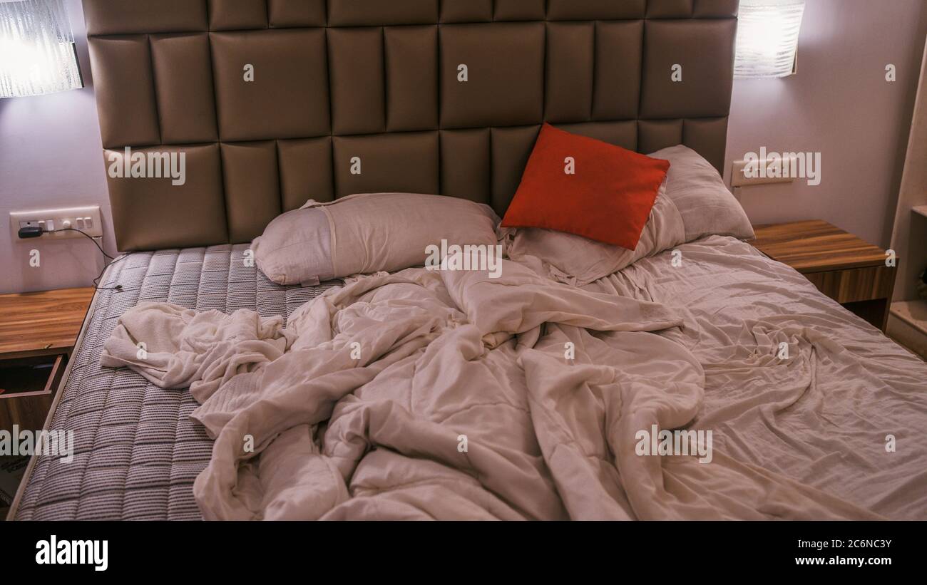 Unmade bed in modern bedroom. From above warm blanket and soft pillows