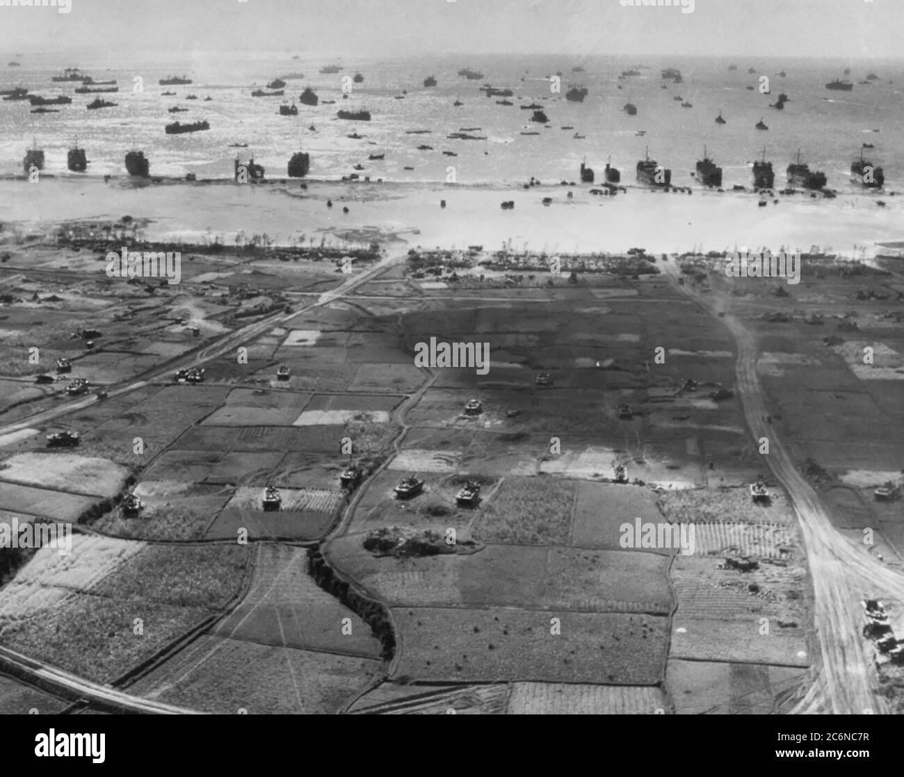 A view of one of the beaches on Okinawa taken by Navy Chief Photographer’s Mate E.W. Peck off USS Tulagi, April 3, 1945. Several tank landing ships and medium landing ships are on the beach with others shipping offshore. Note the tracked landing vehicles in the fields in the foreground. National Archives photo Stock Photo