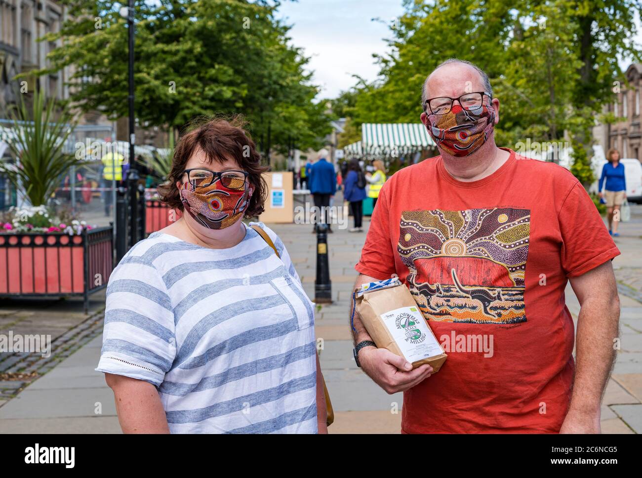 Haddington, East Lothian, Scotland, United Kingdom, 11th July 2020. Farmers Market restarts in Phase 3: the popular monthly outdoor market is held for the first time since lockdown with locals keen to support local food producers. Despite not being mandatory outdoors, most people are  wearing face masks. Laura and Matt have made their own colourful matching face masks and bought a packet of Mungoswells locally milled flour Stock Photo