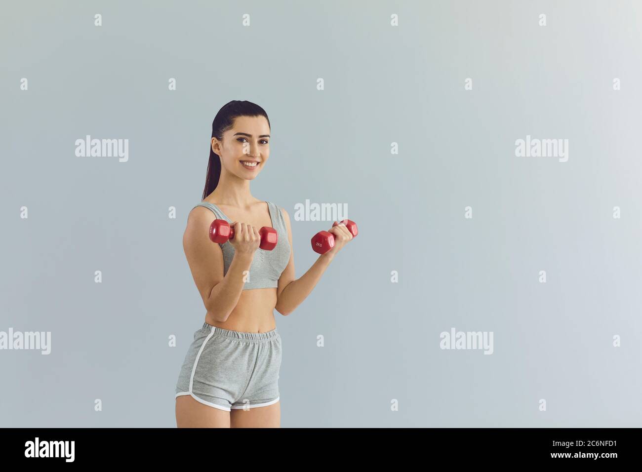 Cheerful fit female athlete training with dumbbells near gray wall Stock Photo