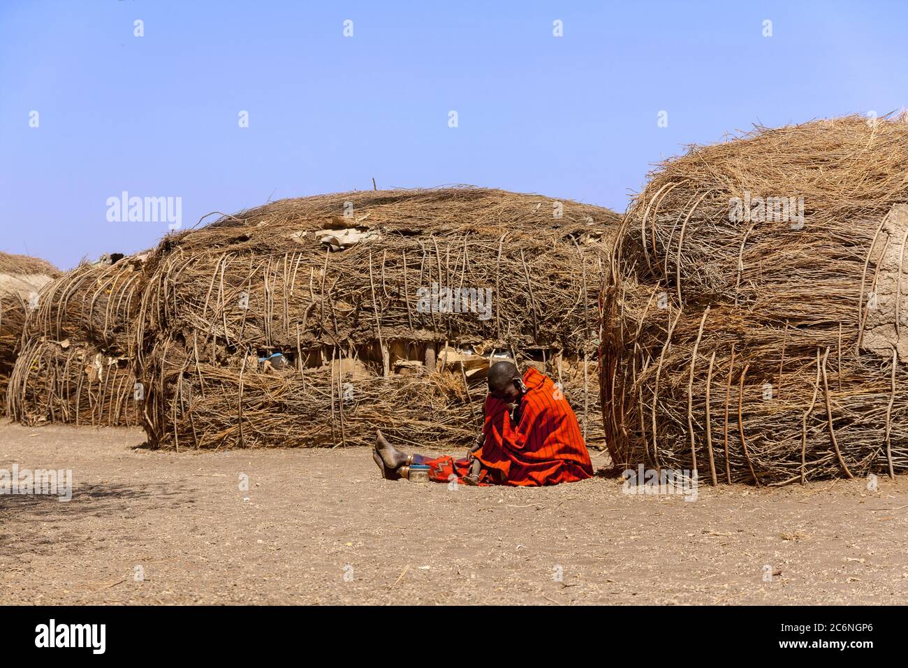 Serengeti, Tanzania - September 21. 2012: A Massai woman in red in front of the traditional huts inside an Massai village in the Serengeti National Pa Stock Photo
