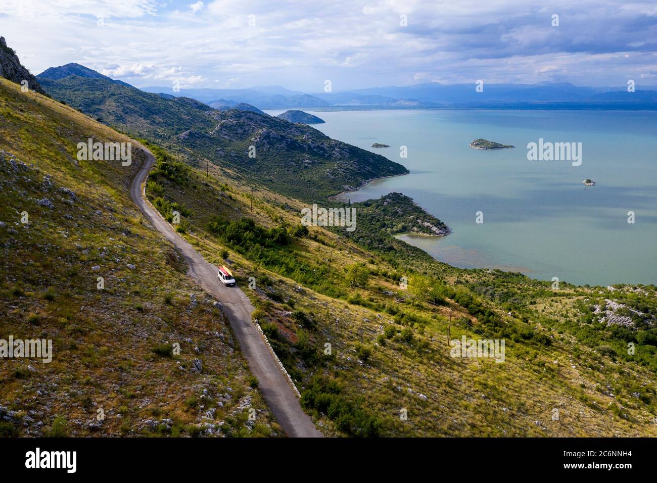 Car carrying two kaykas driving on a narrow mountain road on the edge of a cliff on the southern shore of Skadar Lake, Montenegro Stock Photo