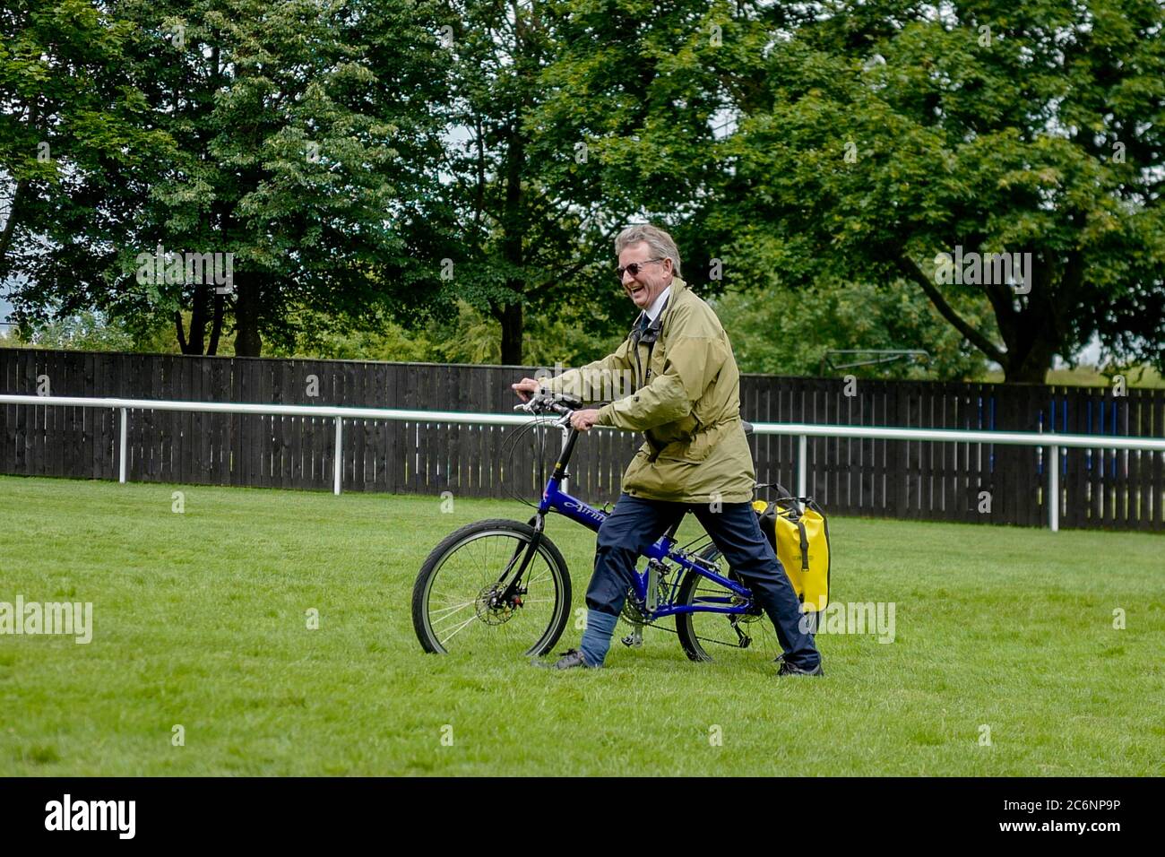 Trainer Mark Johnston arrives on the course with his bicycle after landing his aeroplane further up the enclosures and riding to the grandstands on day three of The Moet and Chandon July Festival at Newmarket Racecourse. Stock Photo