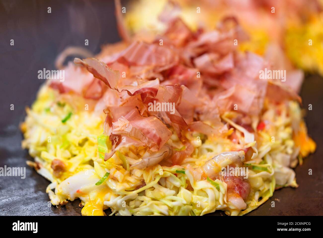 Close-up on an okonomiyaki Japanese omelet, which means cooked to your liking, prepared with shredded cabbage and covered with dried shavings of bonit Stock Photo