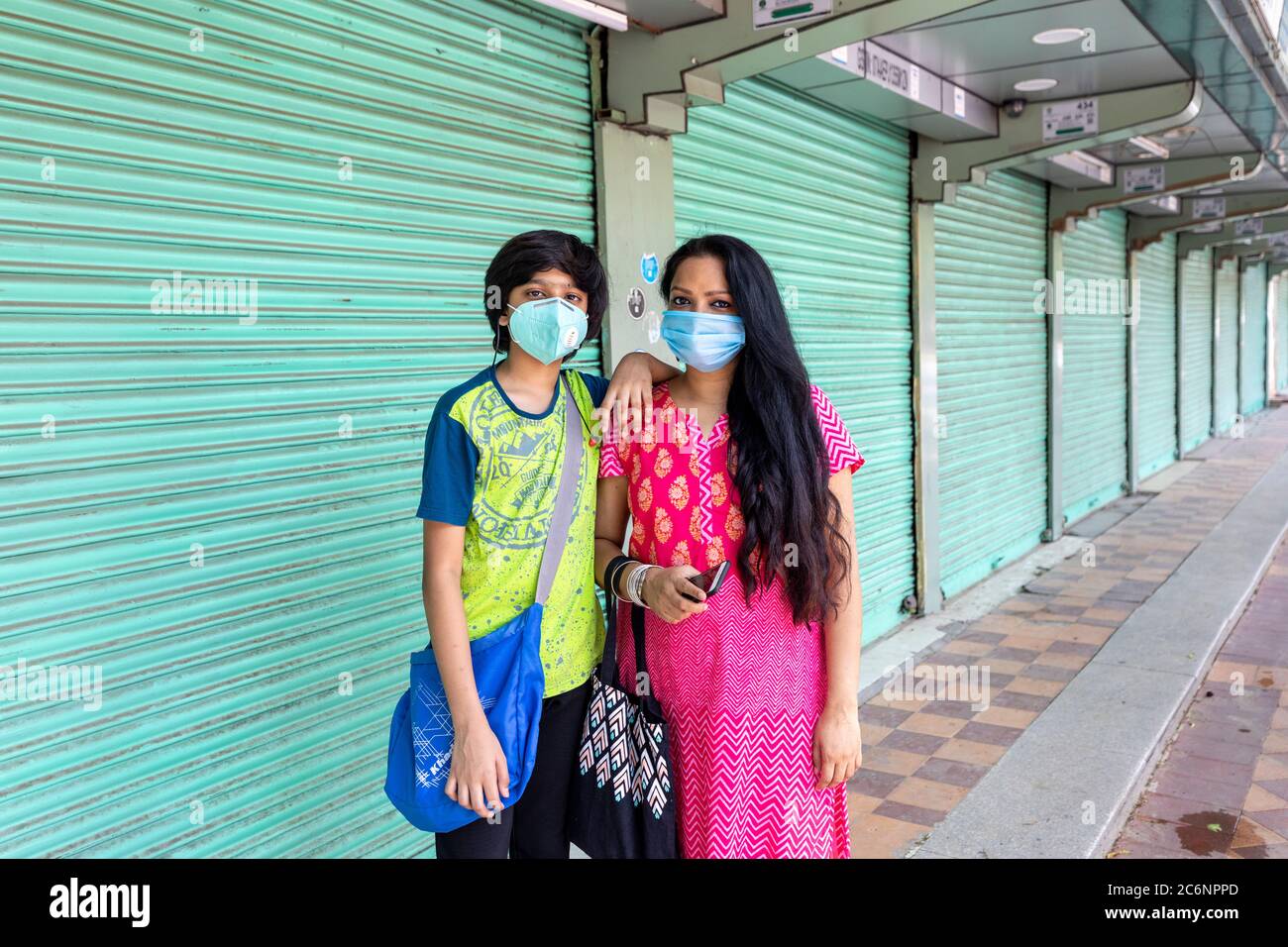 Indian woman and her son wearing corona masks infront of closed shops ...