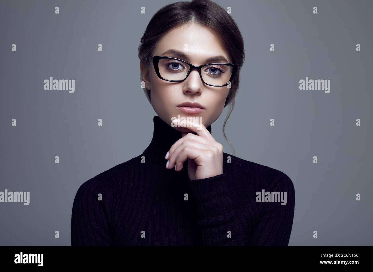 Portrait of cute student girl wearing black turtleneck sweater and stylish eyeglasses posing on gray background in studio Stock Photo