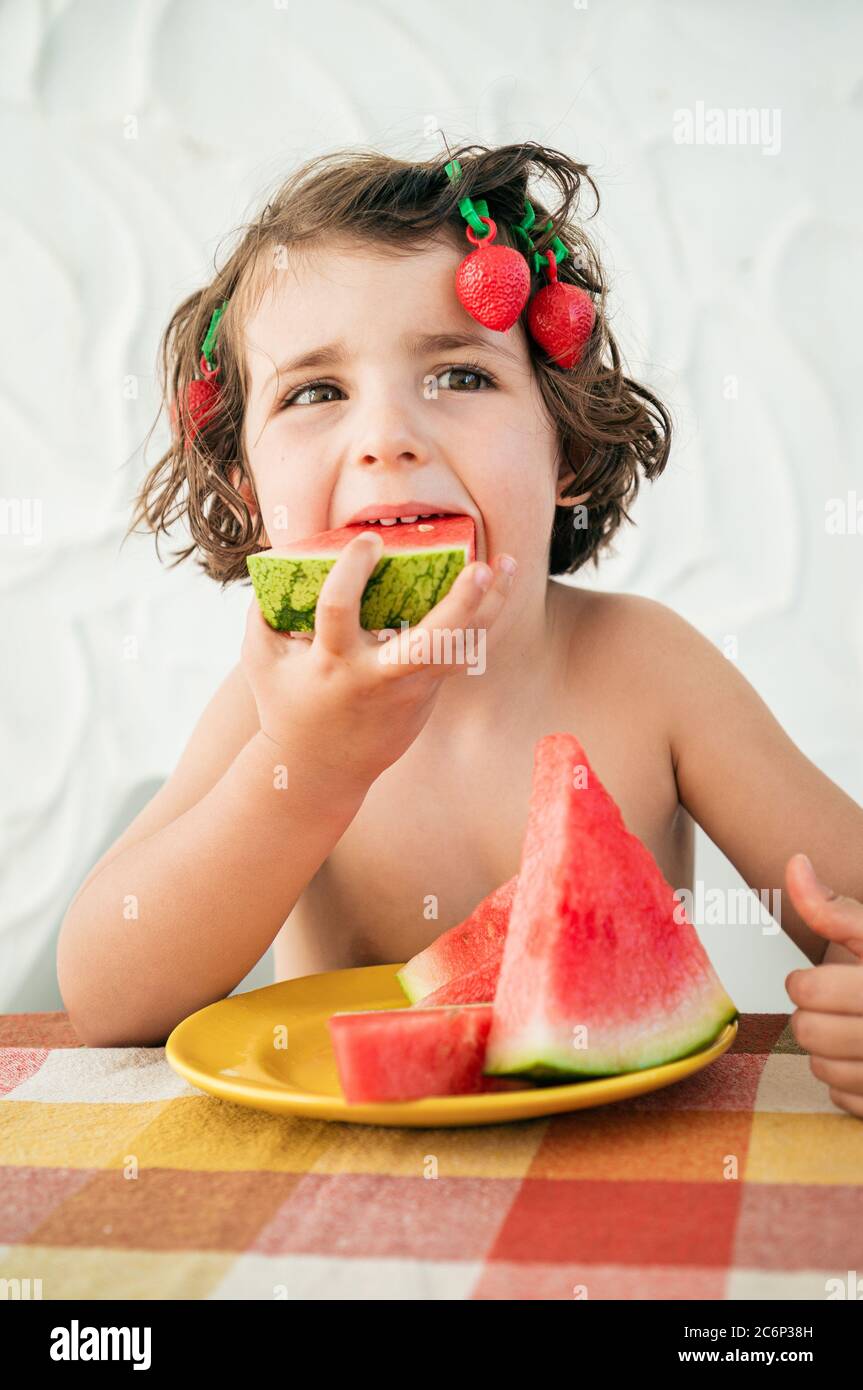 Hungry cute girl devours watermelon slices, refreshing summer dessert. Has strawberry hair clips acting being goofy funny Stock Photo