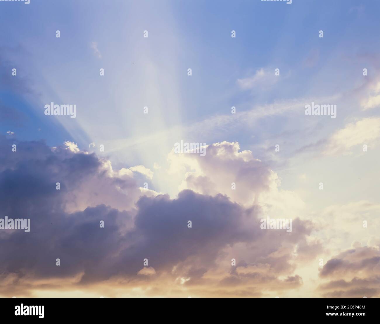 Sun rays coming out from behind clouds with blue sky above Stock Photo
