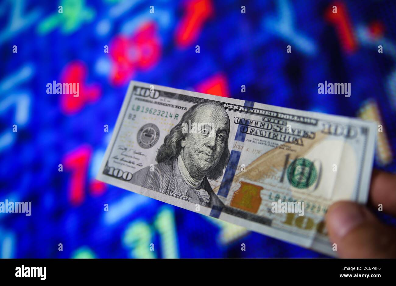Investment withdrawal concept: View on hand holding one 100 dollar note, blurred stock market exchange board background. (Focus on face) Stock Photo