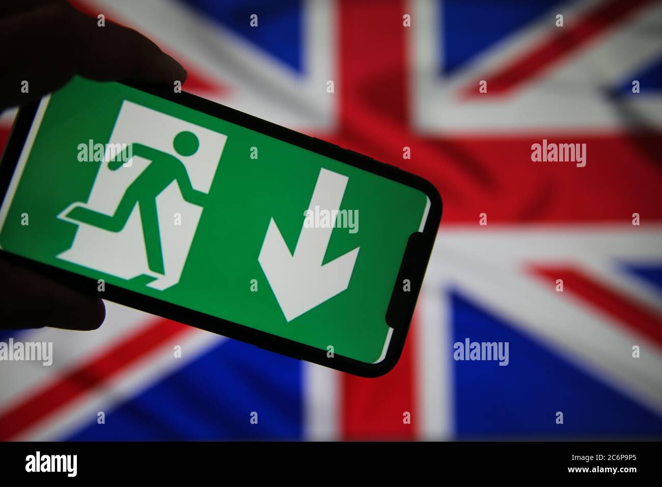 Viersen, Germany - July 9. 2020: View on isolated mobile phone screen with green emergency evacuation exit sign. Blurred union jack background. Stock Photo