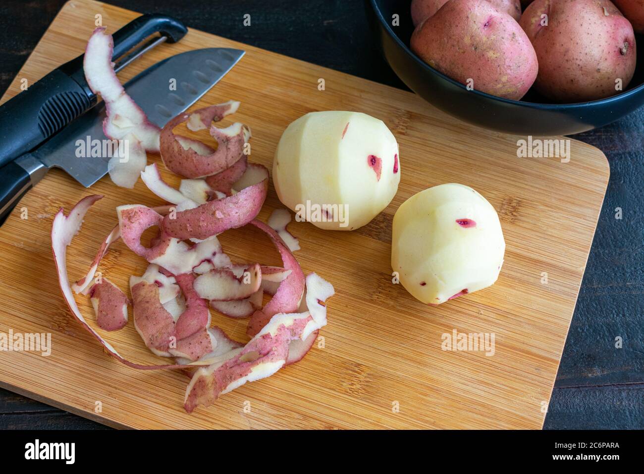 Peeling Red Potatoes on a Bamboo Cutting Board: Raw potatoes with a vegetable peeler and kitchen knife on a wood cutting board Stock Photo