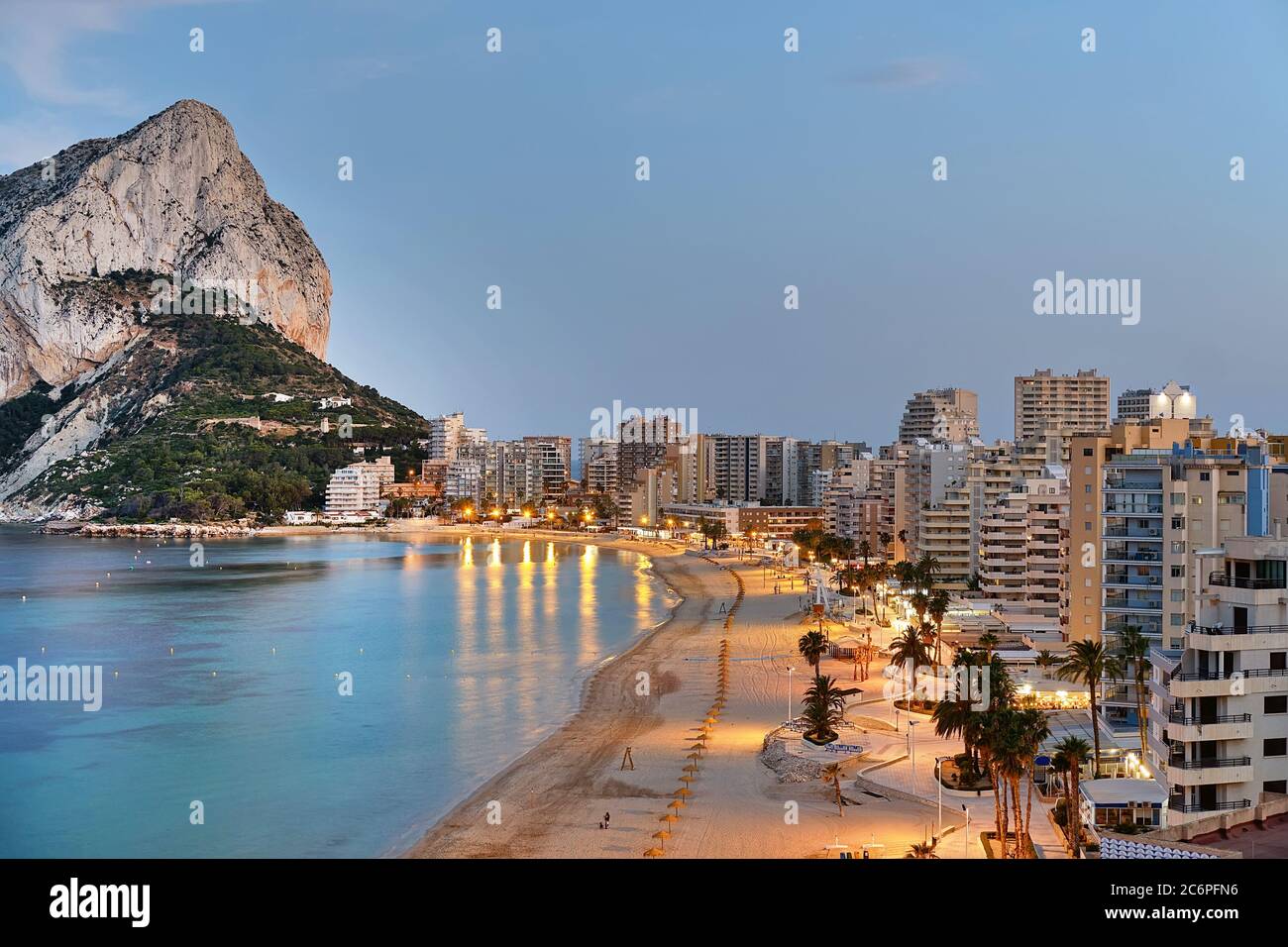 Panoramic view from above of Calpe cityscape. Street lights illuminating seafront promenade during sunset. Empty sandy beach and rocky mountain Ifach Stock Photo