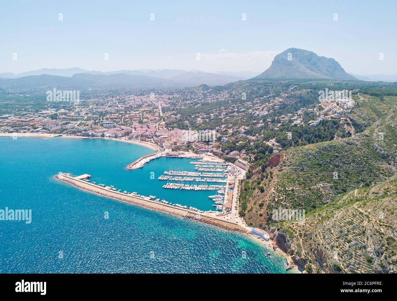 Aerial photo drone point of view coastal town of Javea with green mountains, turquoise bay Mediterranean Sea moored vessels in harbour, Spain Stock Photo