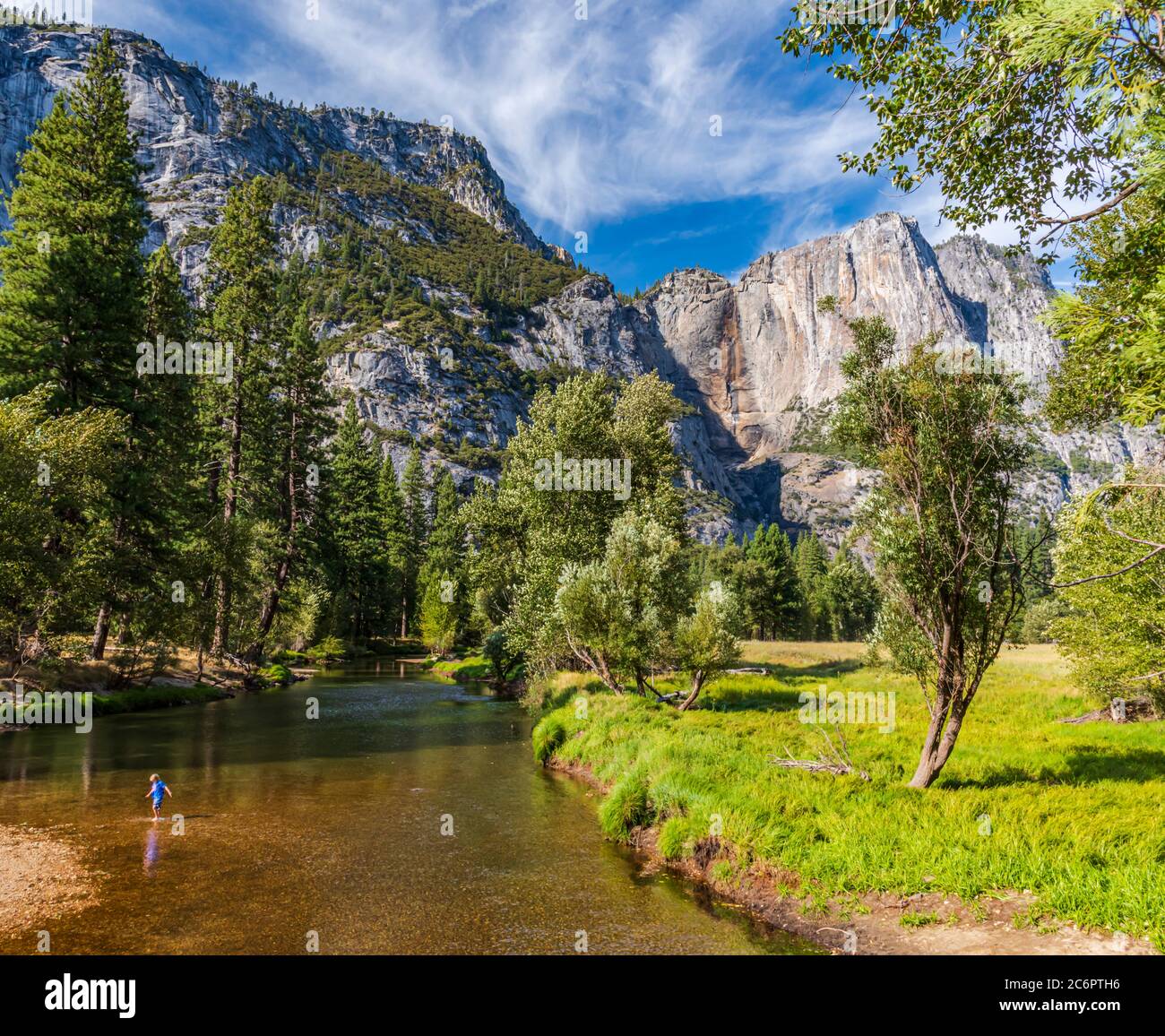 A child is playing in the waters of the Merced River as it flows through Yosemite Valley and the canyon walls form a grand backdrop. Stock Photo