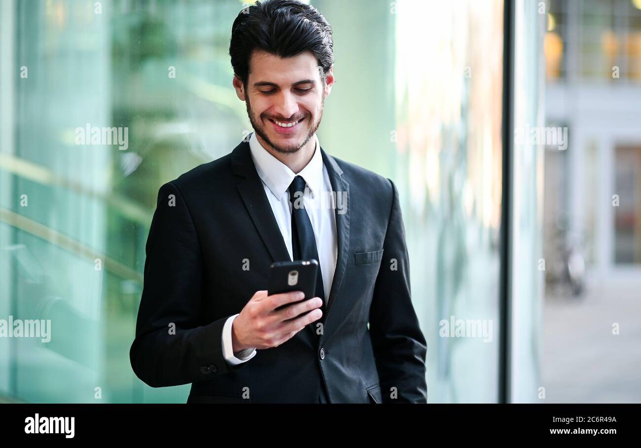 Handsome young manager using a smartphone outdoor Stock Photo - Alamy