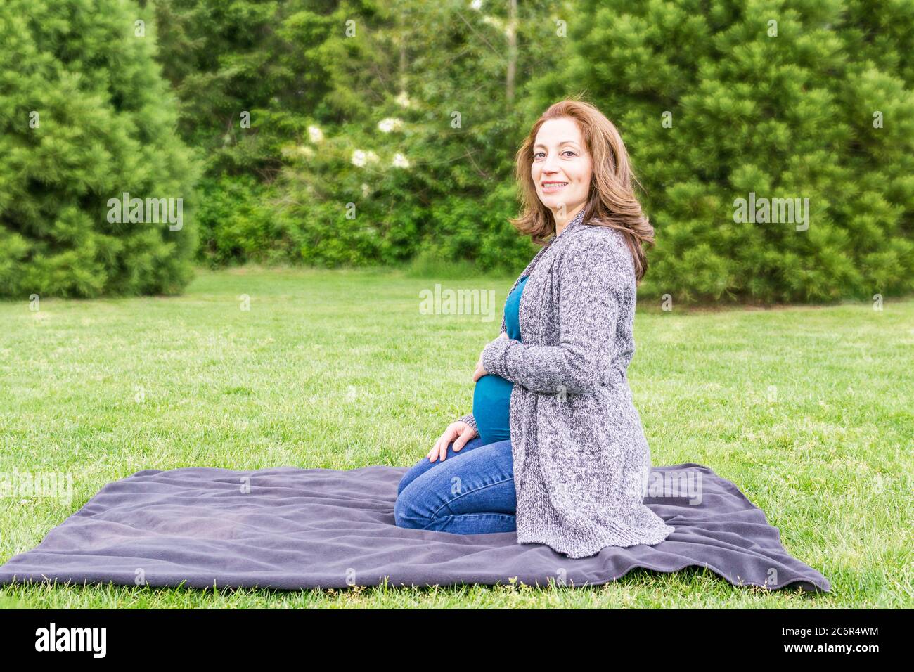 Happy pregnant caucasian woman relaxing in a park holding hands on her ...