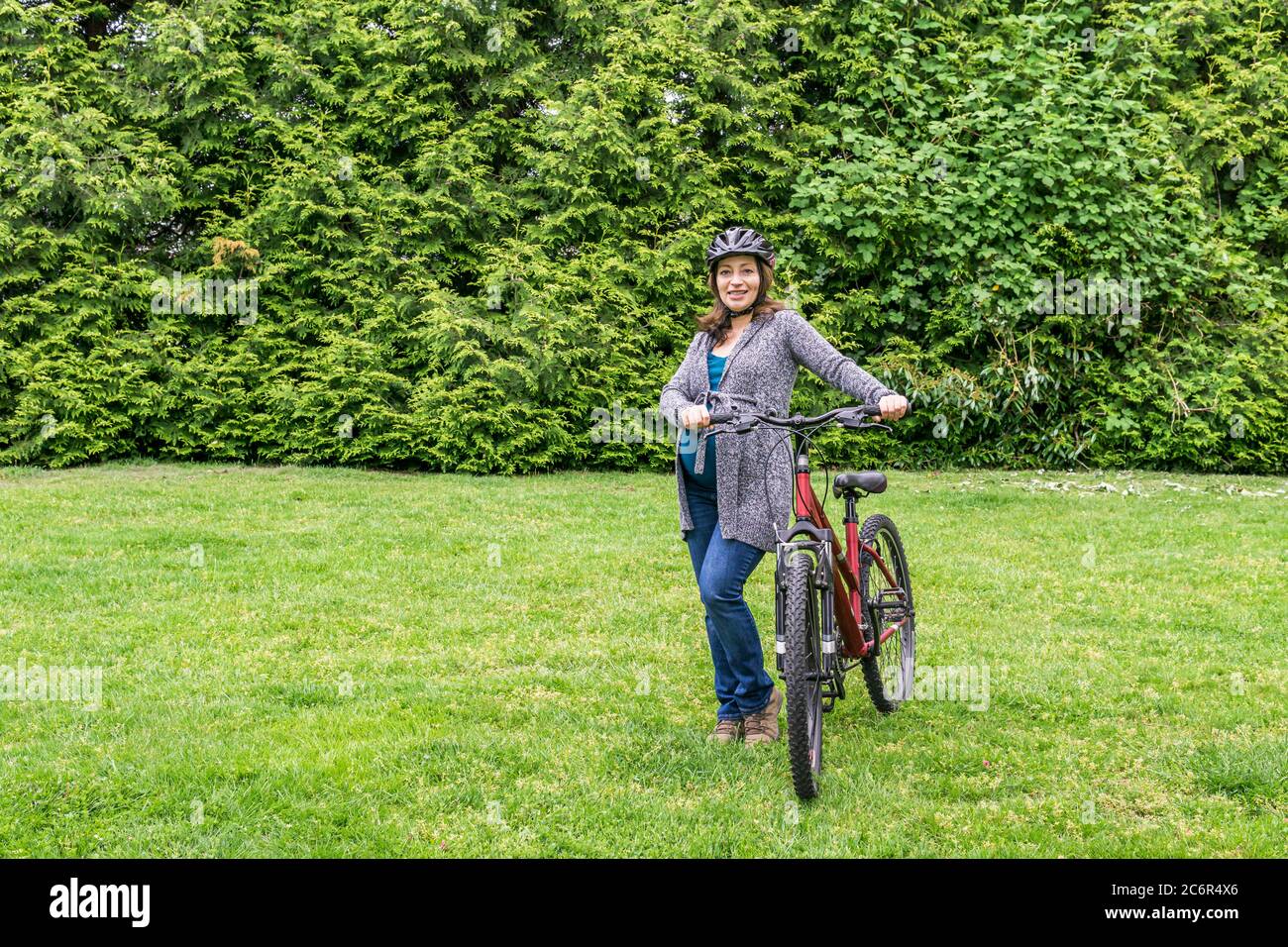 pregnant woman on the green lawn in a park holding bicycle ready to