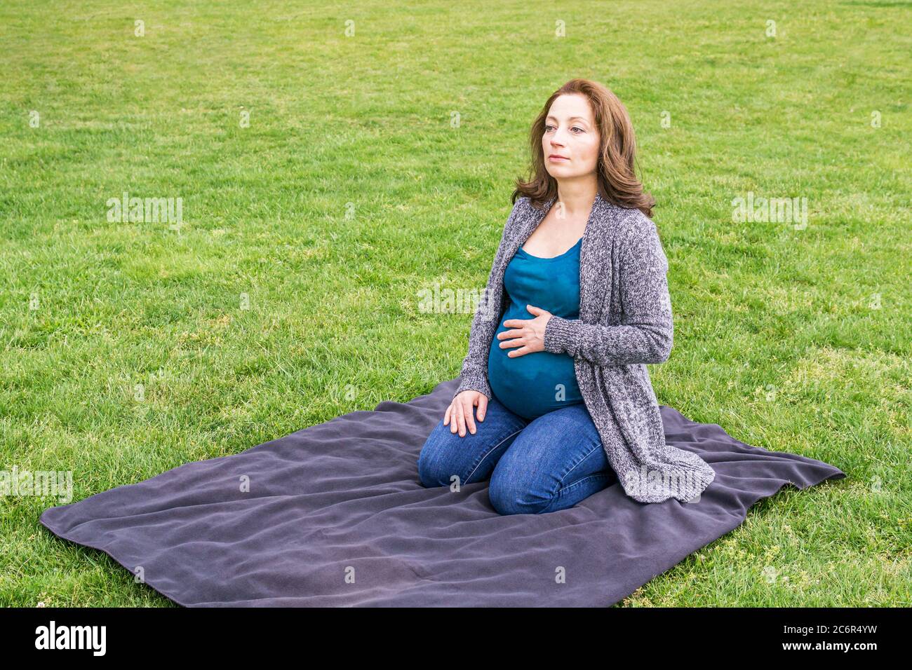 Happy pregnant caucasian woman relaxing in a park holding hands on her ...