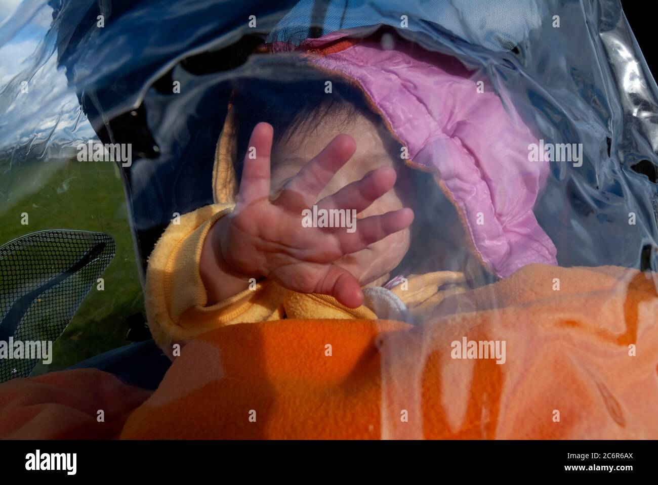 Toddler sitting in stroller covered with plastic. Stock Photo