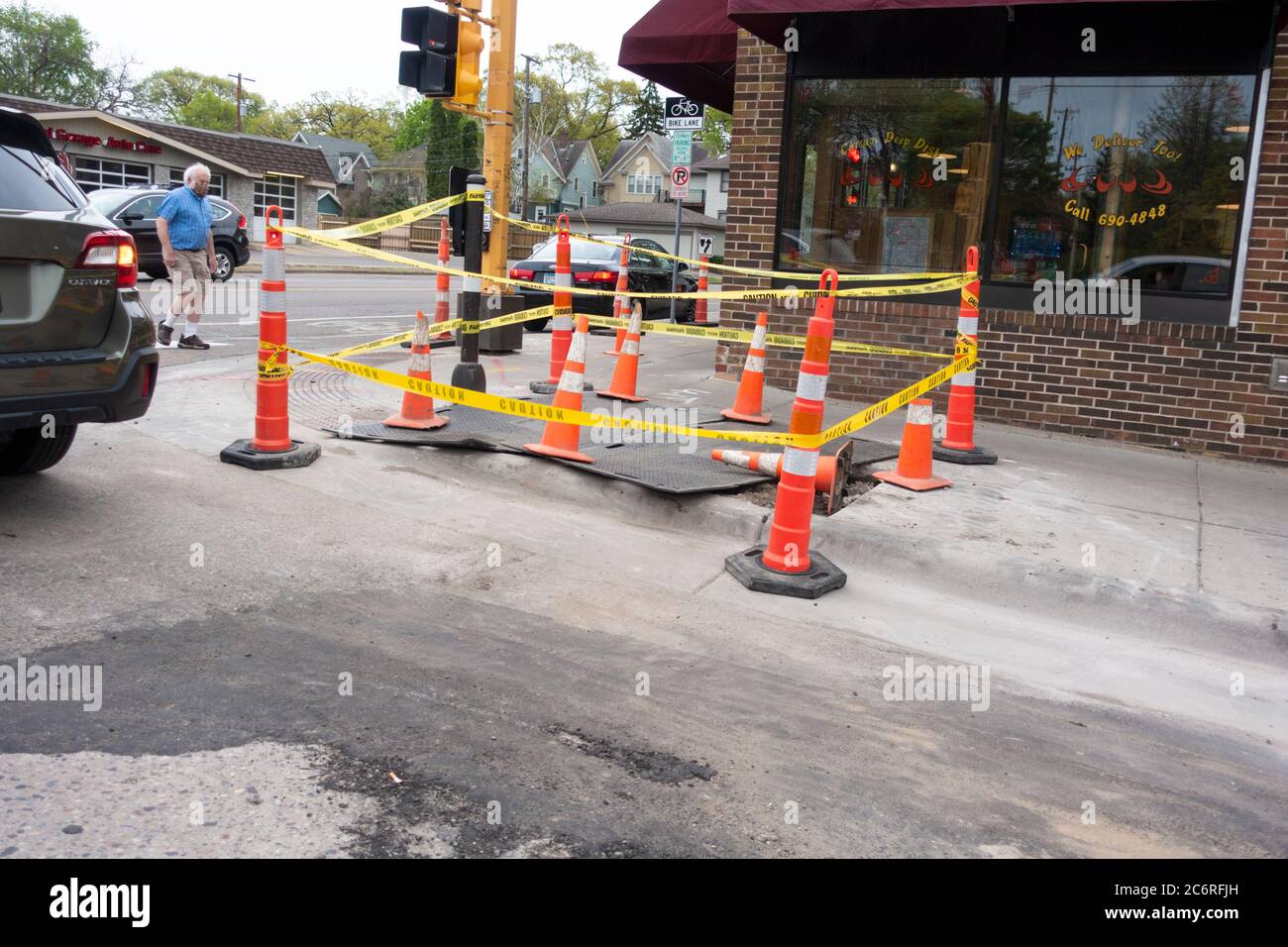 Orange cones and yellow caution tape surround large sidewalk repair