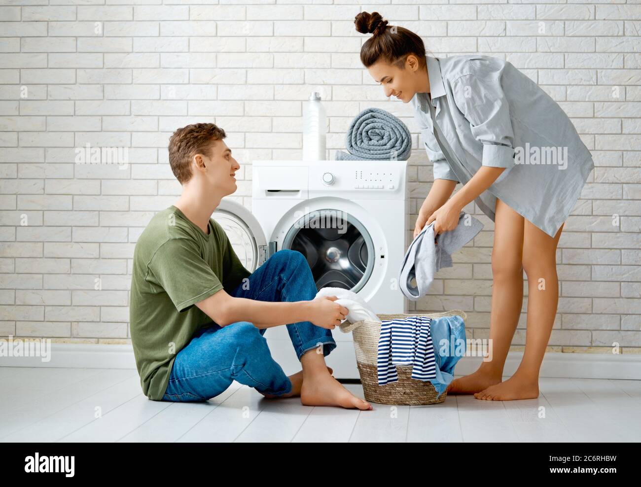 Beautiful young loving couple is smiling while doing laundry at home ...