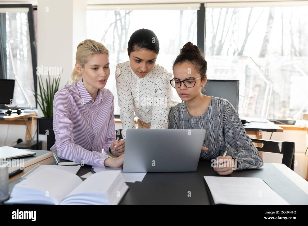 Focused multiracial female employees work on laptop together Stock Photo