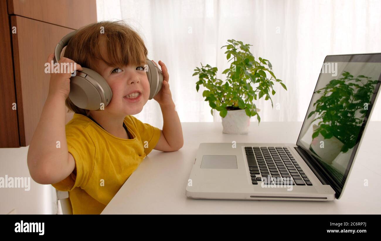 Kid puts on headphones in front of a laptop Stock Photo
