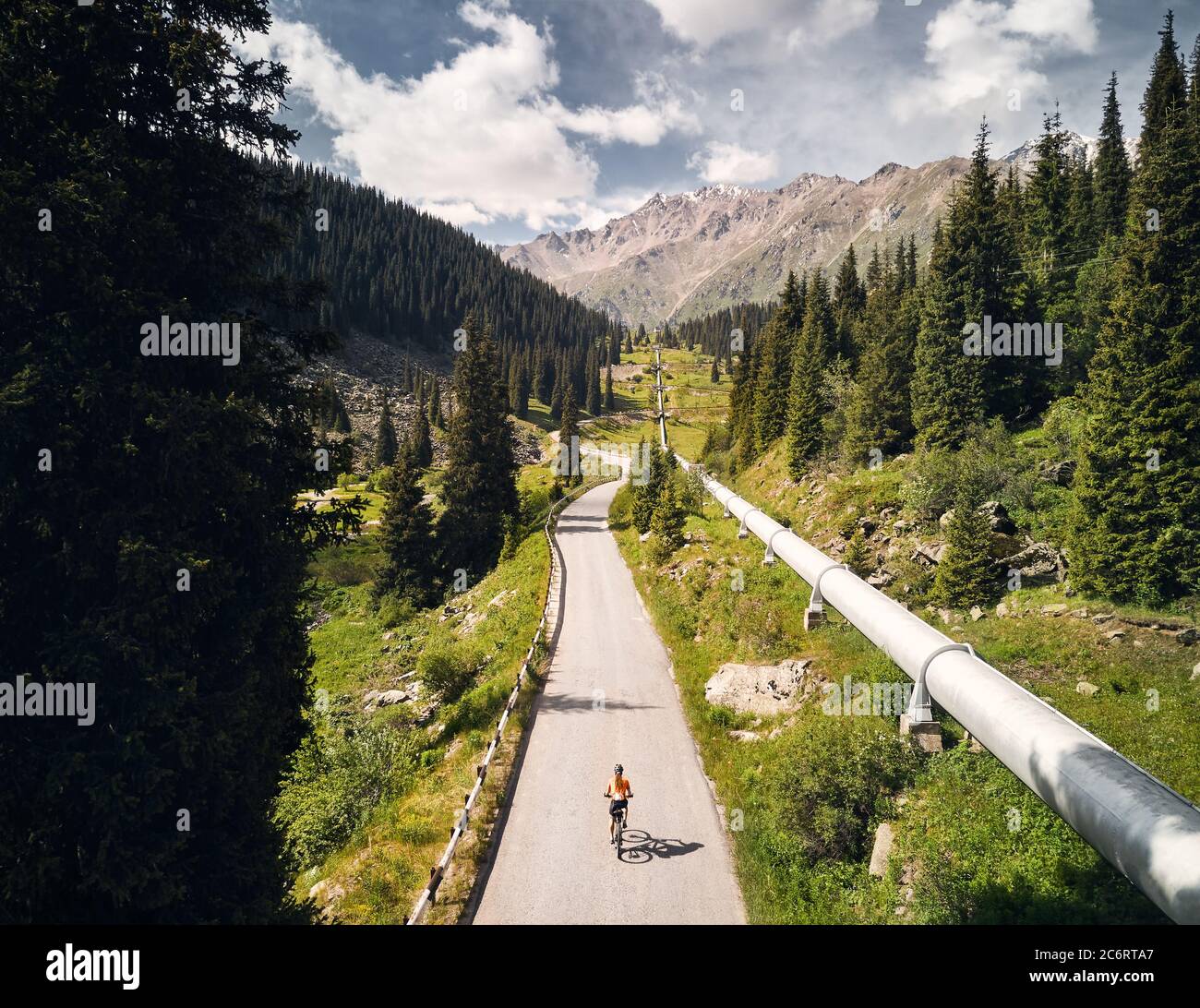 Man on mountain bike rides on the road to the mountain valley against blue cloudy sky. Recreation and healthy lifestyle concept. Stock Photo