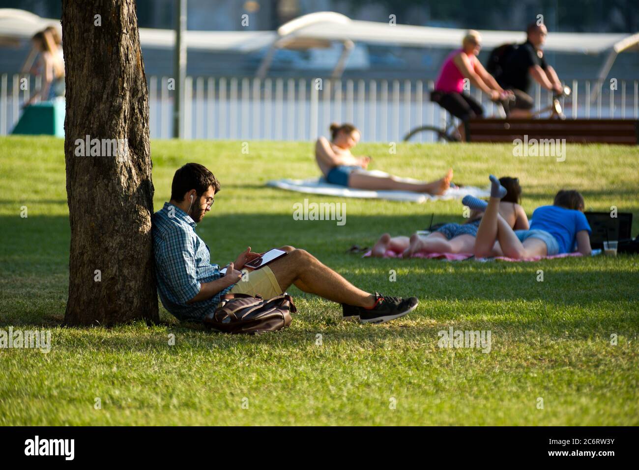 Bearded young man reads sitting on grass in a park Stock Photo