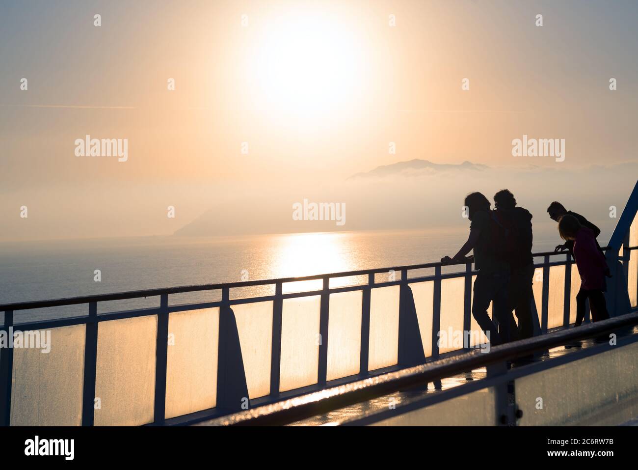 Silhouette of travelers on a ship deck watching sunrise and coastline ...