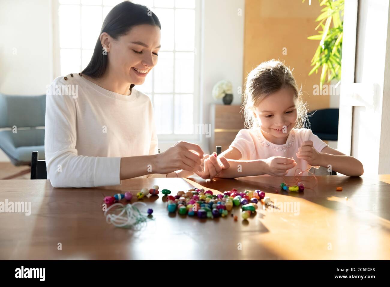 Smiling mother and adorable little daughter making colorful beads
