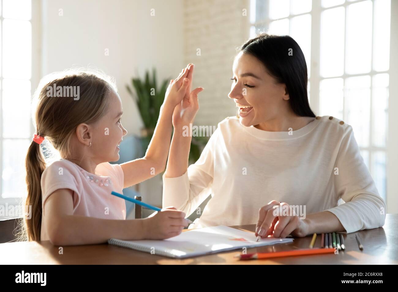 Happy mother and little daughter giving high five, drawing pencils Stock Photo