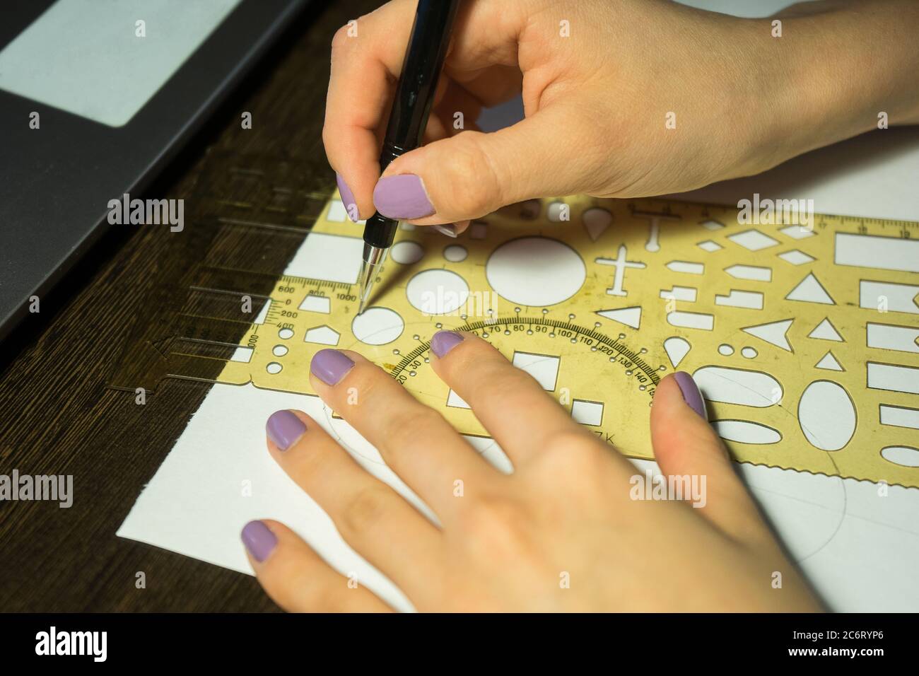 Girl with purple nails draws a circle with a ruler with figures Stock Photo