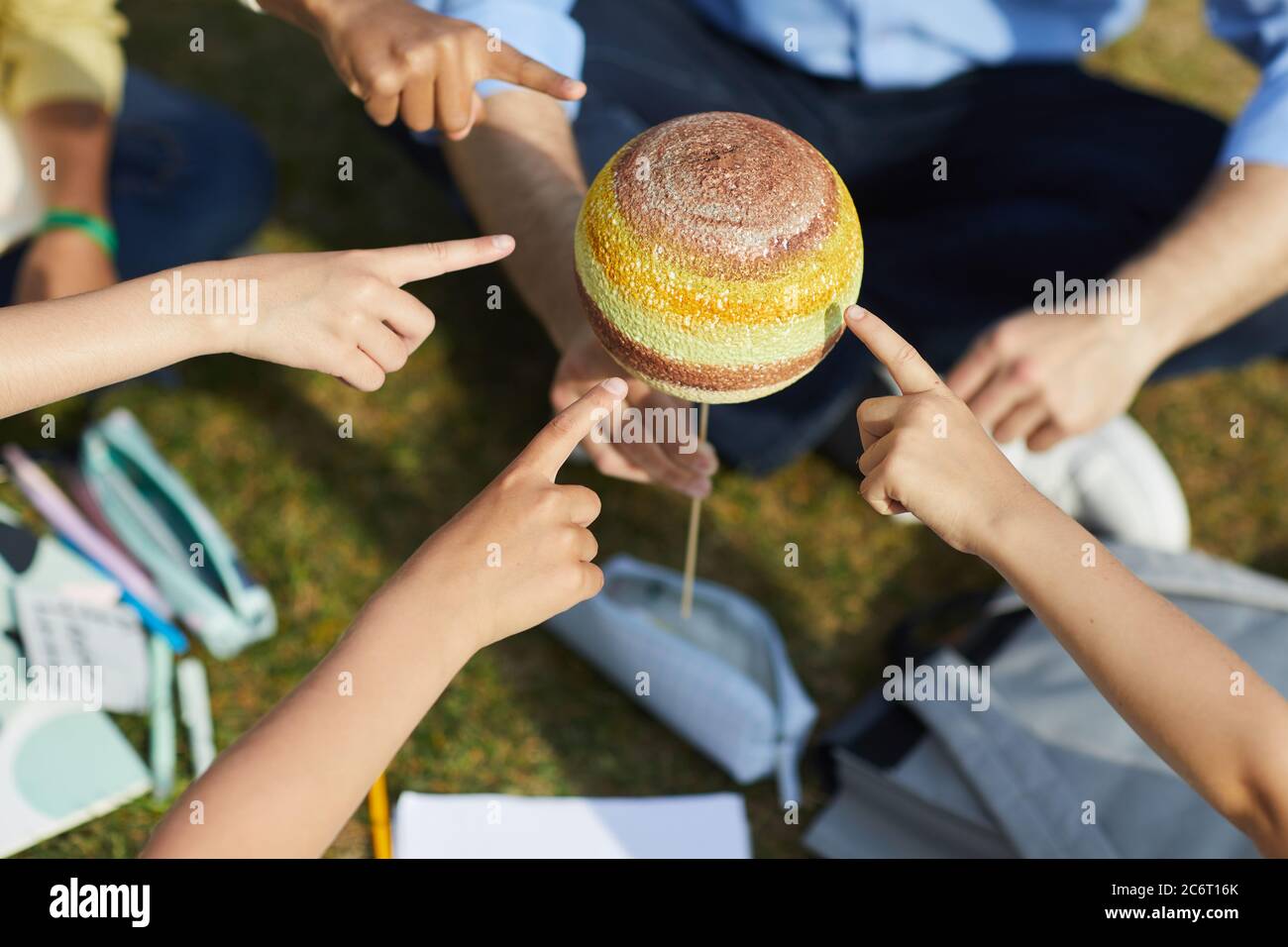 Top view close up of group of children pointing at model planet while enjoying outdoor astronomy class in sunlight, copy space Stock Photo