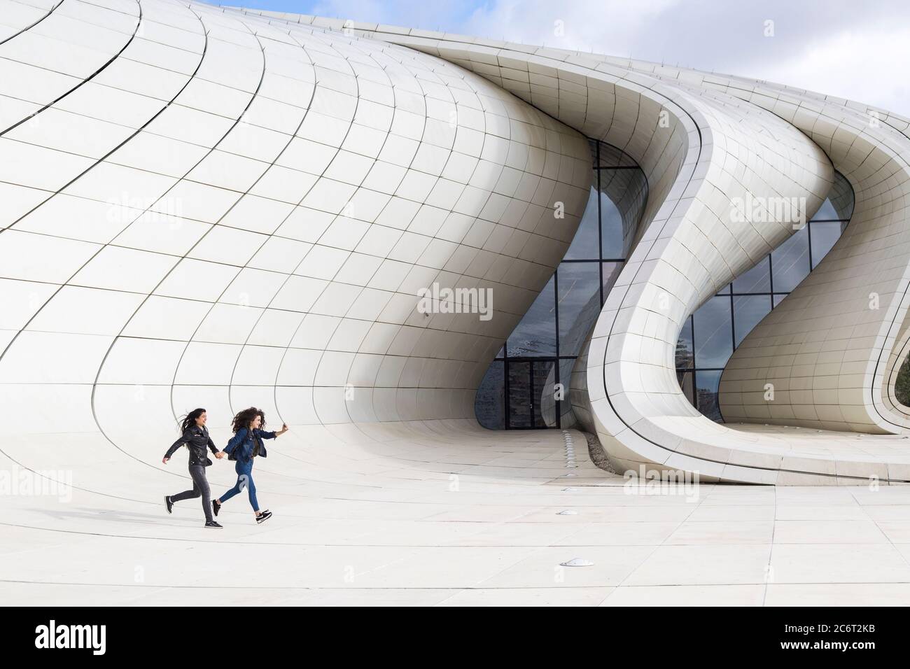 Two teenage girls running up the front of the Heydar Aliyev center, designed by Zaha Hadid the centerpiece of modern architecture in Baku Azerbaijan Stock Photo