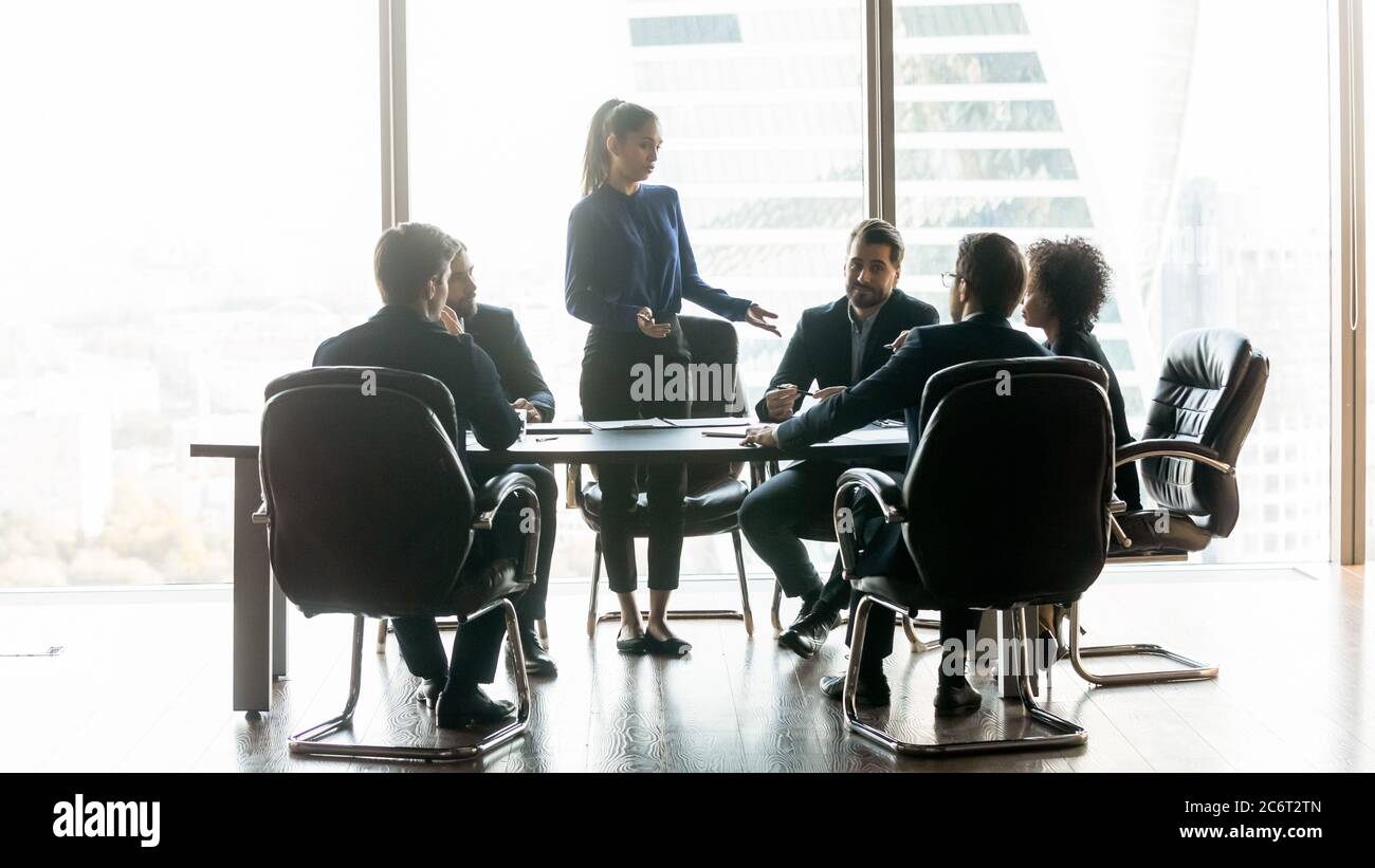 Young business woman standing at table, talking to diverse colleagues. Stock Photo