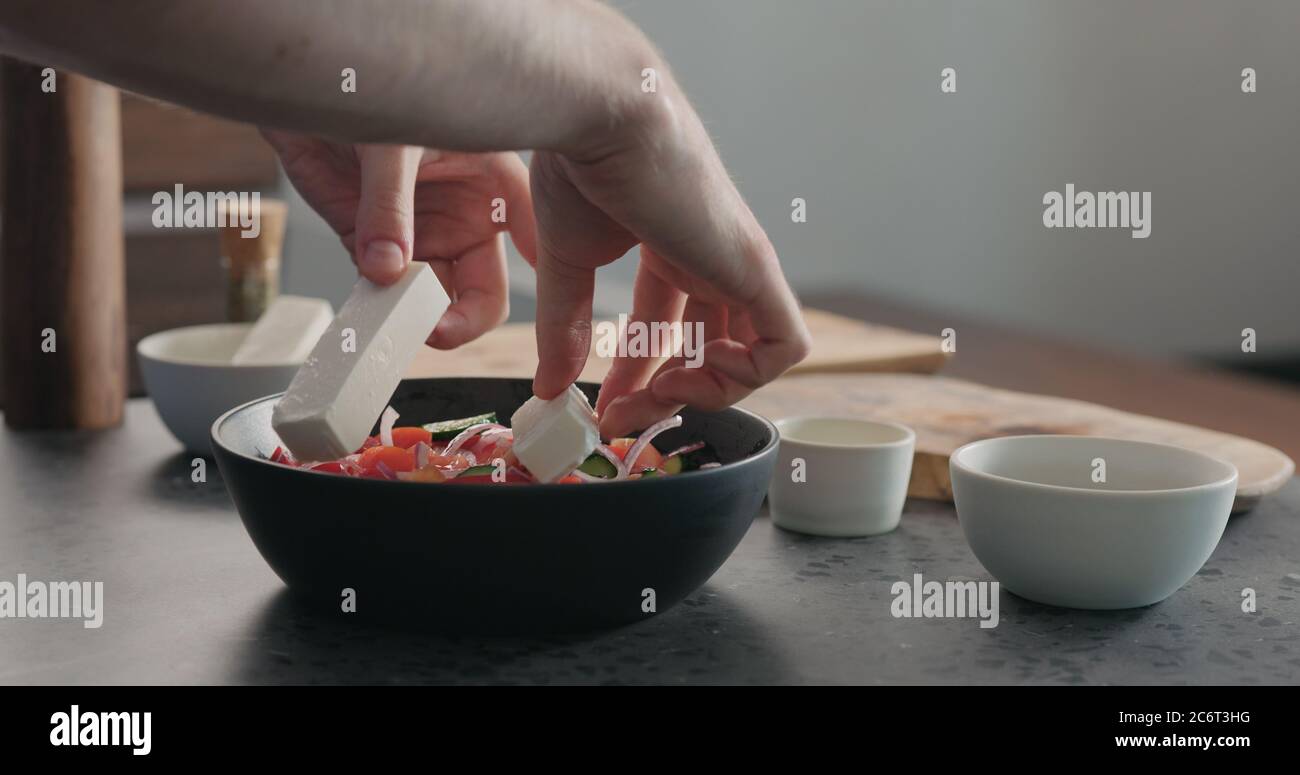 man put feta cheese into greek salad in black bowl Stock Photo