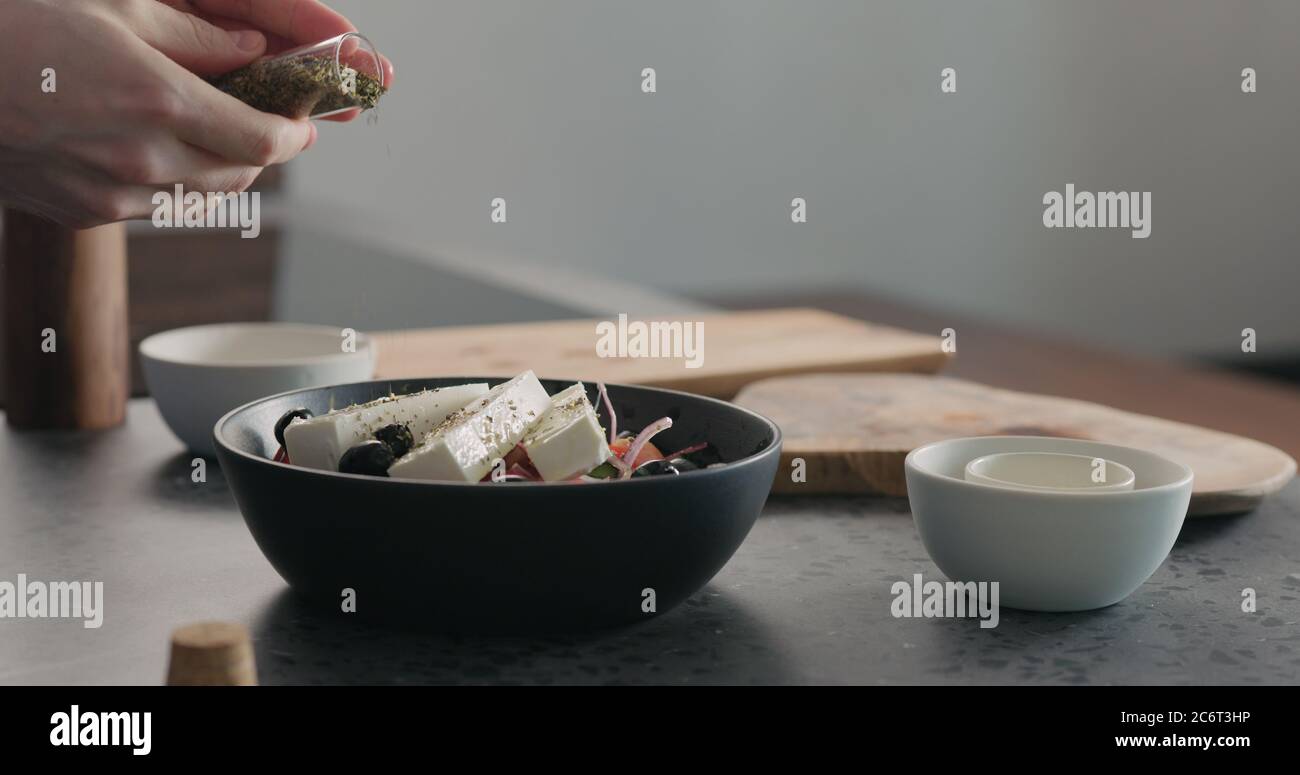 man add spices in greek salad in black bowl Stock Photo