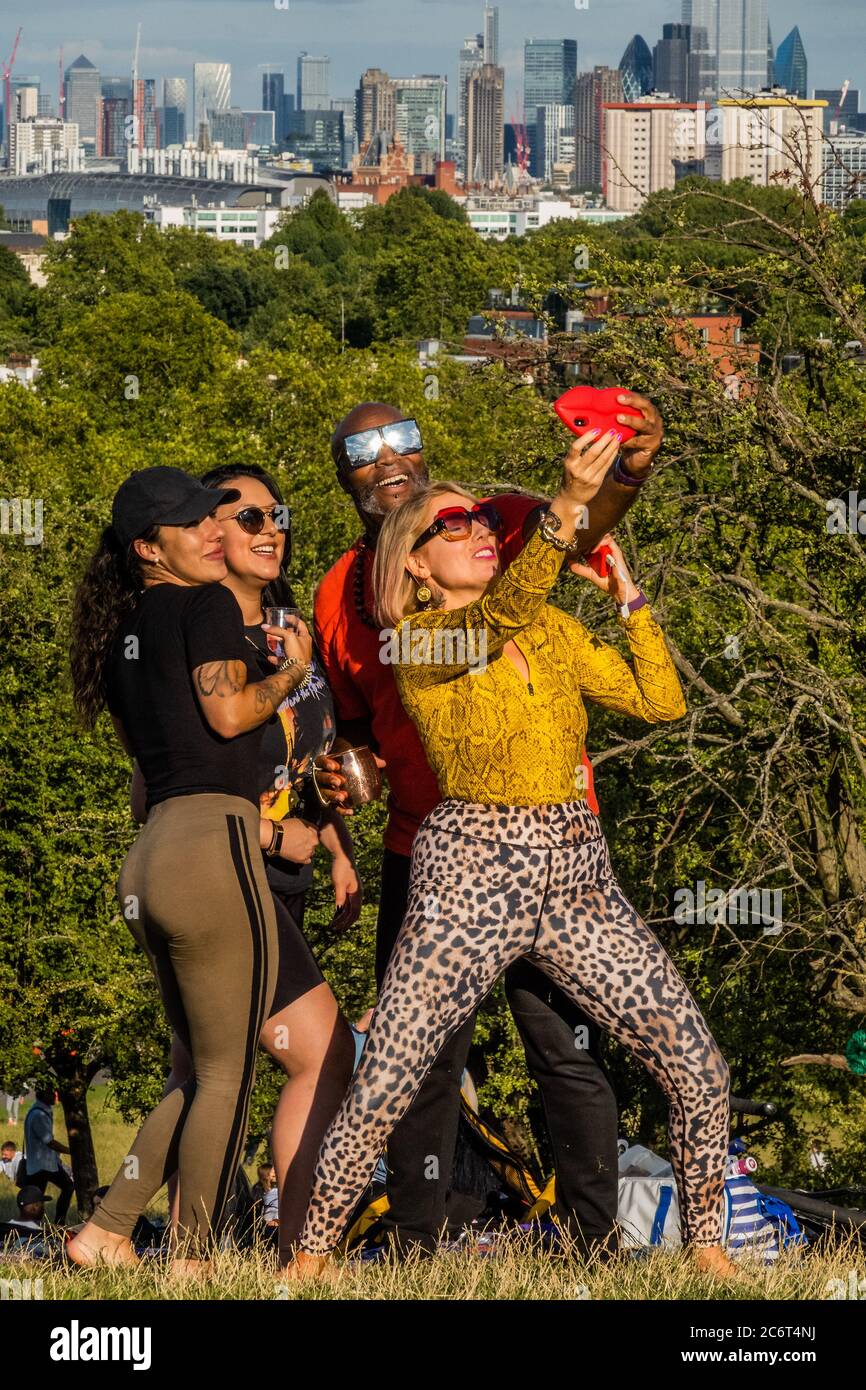 London, UK. 11th July, 2020. No masks, no social distancing, but a selfie - People enjoy a sunny evening on Primrose Hill overlooking the city. The 'lockdown' continues to be eased for the Coronavirus (Covid 19) outbreak in London. Credit: Guy Bell/Alamy Live News Stock Photo