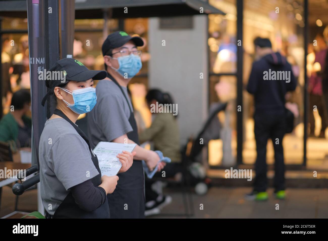 Restaurant staff wearing face mask to avoid covid-19 coronavirus, standing outside restaurant. Blur customers background Stock Photo