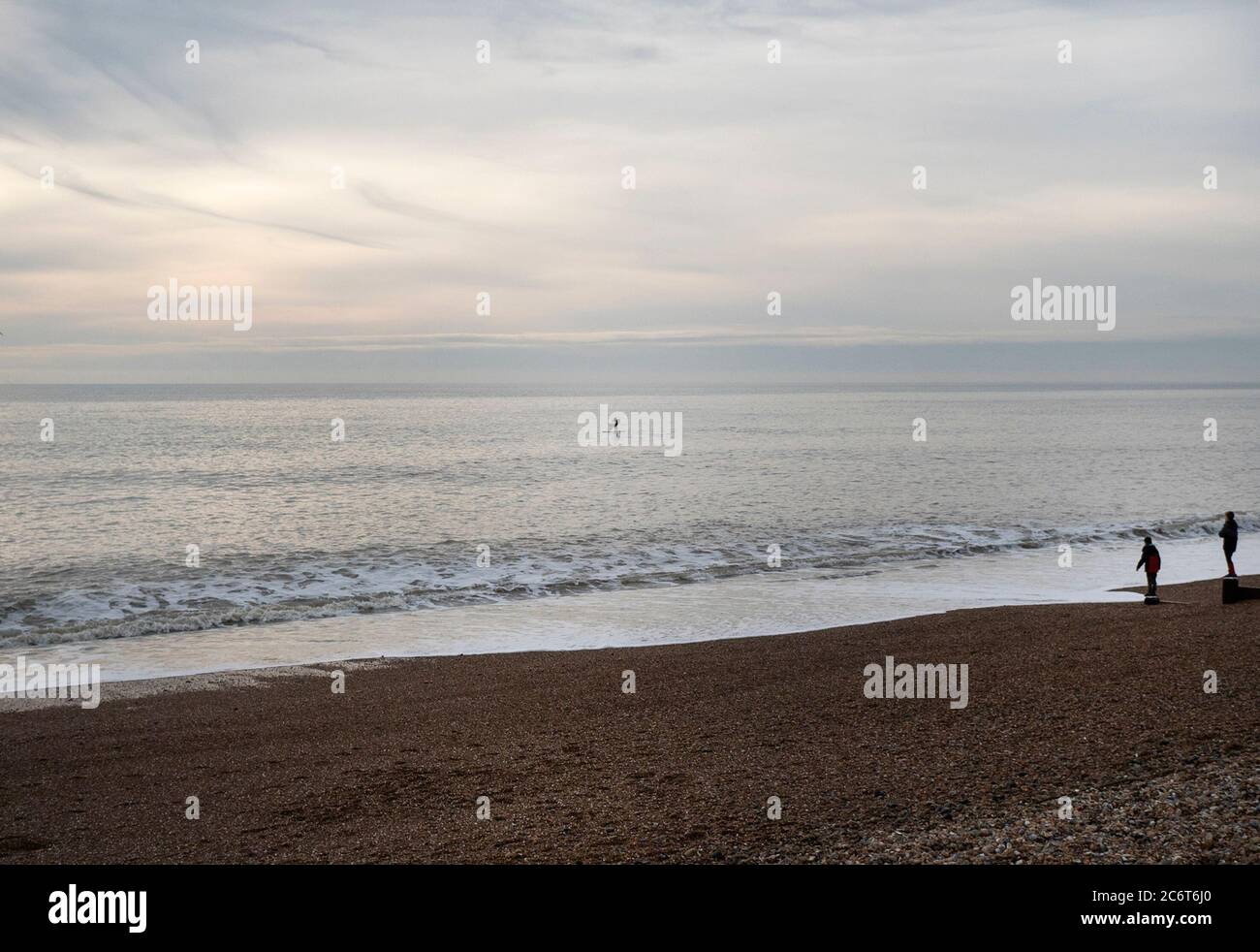 Two People Watching A Paddleboarder In The Early Evening Light Off The Coast At Brighton, East Sussex, UK Stock Photo