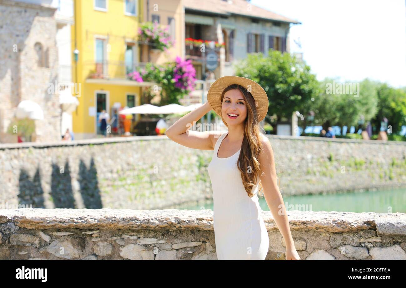 Holidays in Italy. Beautiful fashion tourist girl with hat and white dress enjoying walking in Sirmione town, Italy. Stock Photo